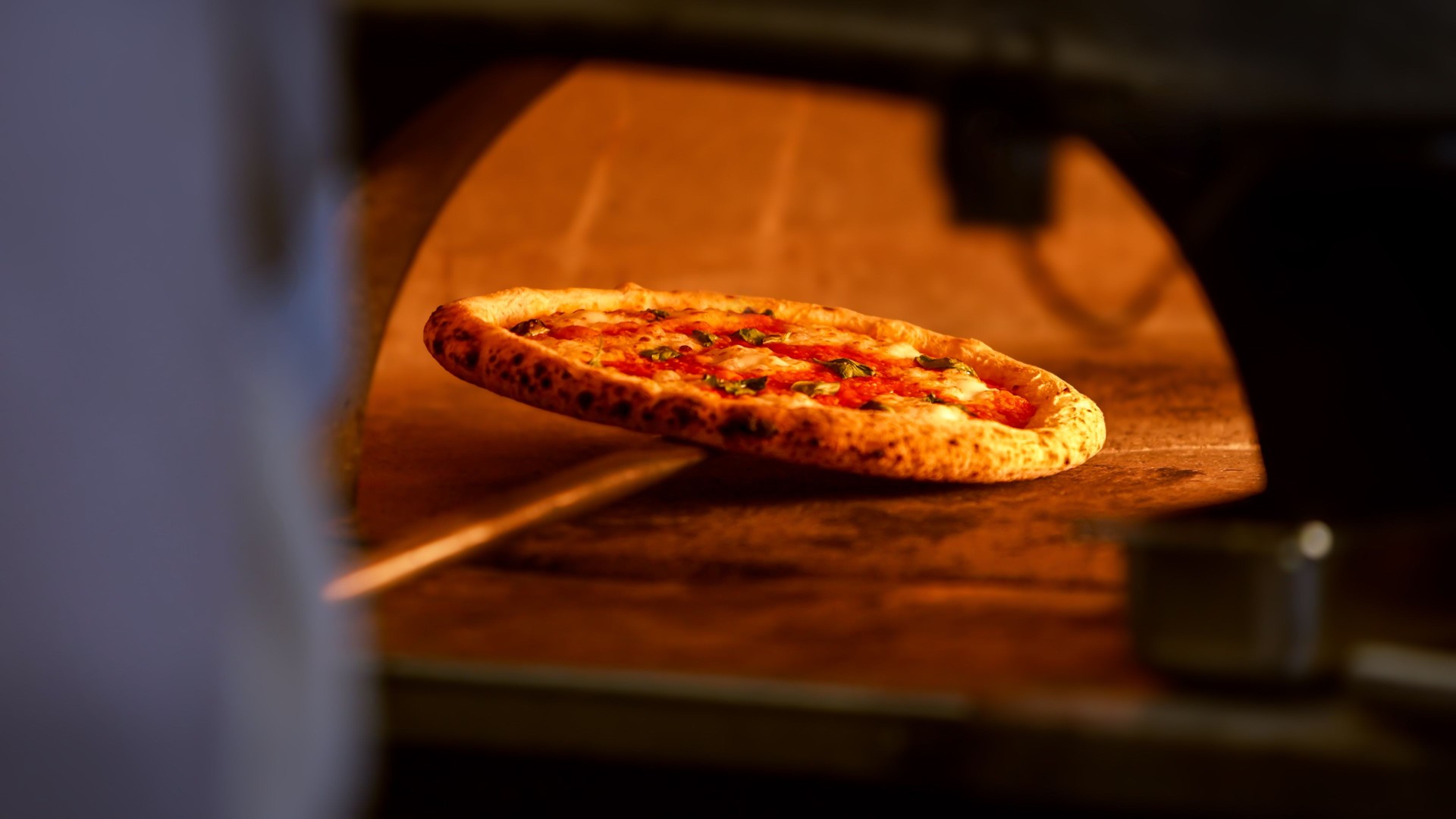 A pizza is baking on a stone in a traditional brick oven, surrounded by flames